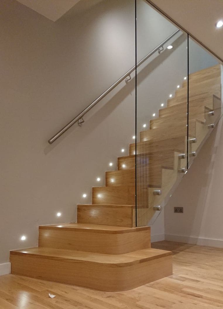 A super modern cut string oak staircase in North Riding with full height bolted frameless glass & wall lights.