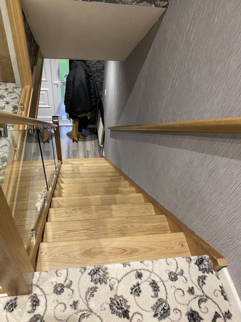 An oak & glass staircase renovation in Halifax with clamped glass with matching polished steel glass clamps and newel caps.