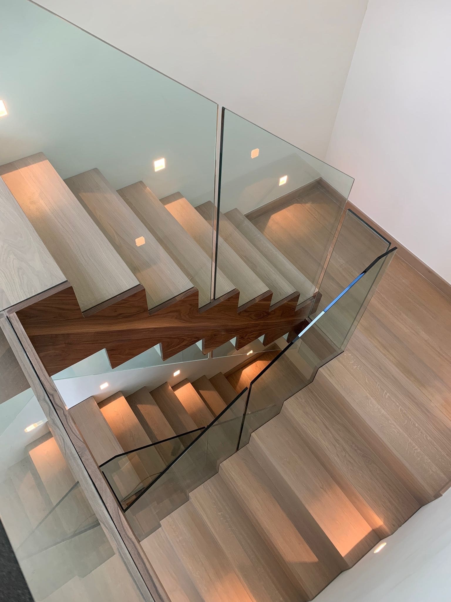 A mesmerising double cut string zigzag staircase in St Albans comprising a combination of walnut, stained oak & white timber with 15mm frameless glass balustrade.