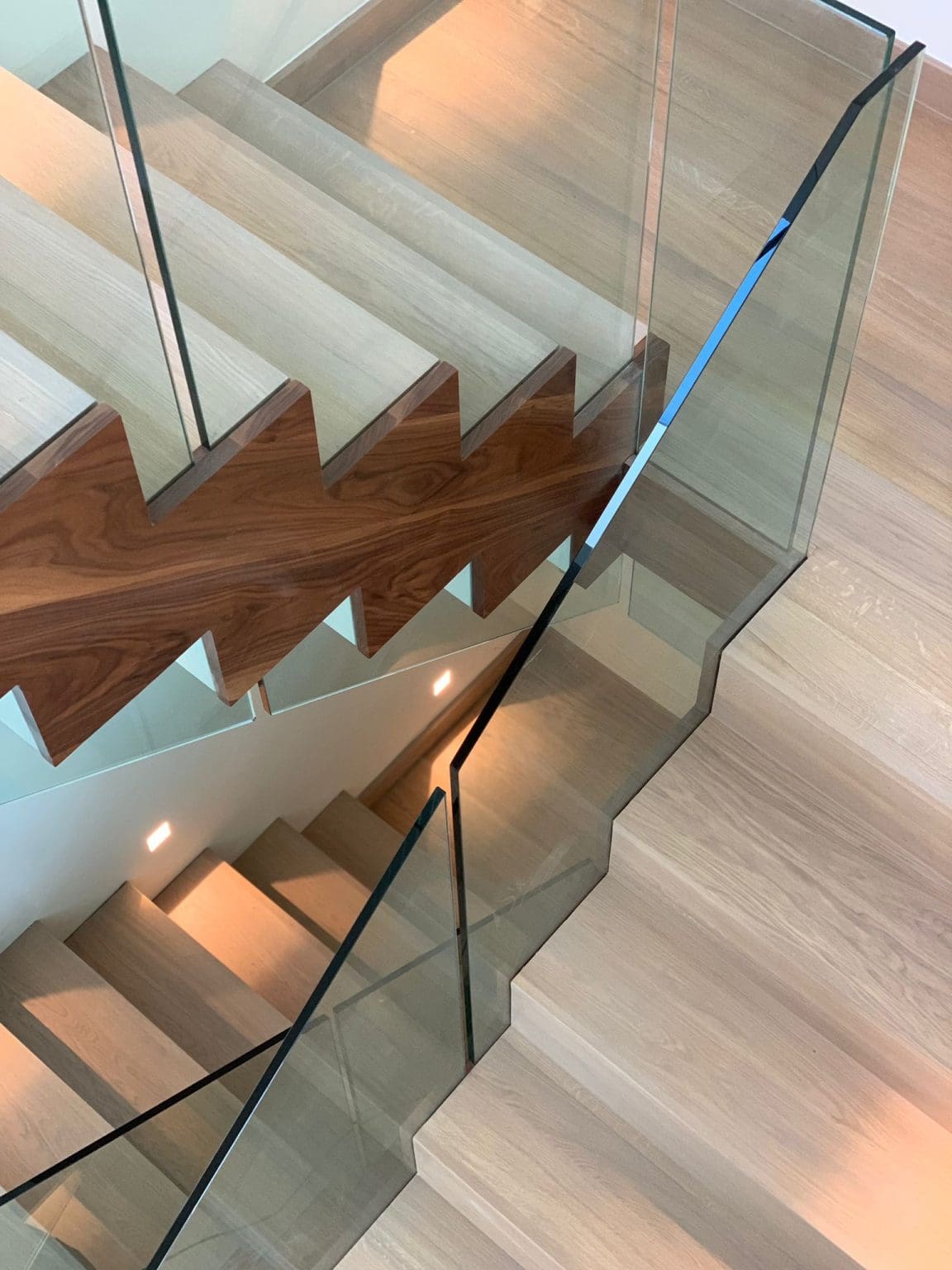 A mesmerising double cut string zigzag staircase in St Albans comprising a combination of walnut, stained oak & white timber with 15mm frameless glass balustrade.