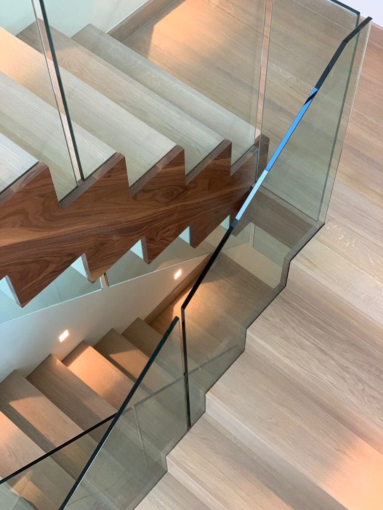 A mesmerising double cut string zigzag staircase in St Albans comprising a combination of walnut, stained oak & white timber with 15mm frameless glass balustrade.