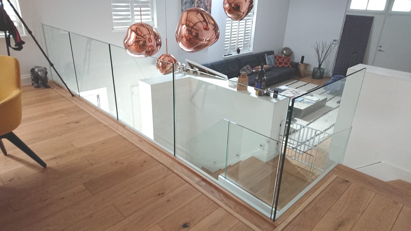 A white frameless glass staircase in a large open plan Lewisham living space.