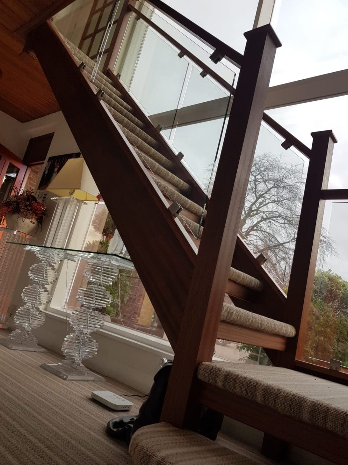 A new staircase with deep, warm tones of sapele paired with clamped glass and softened with a modern striped carpet.