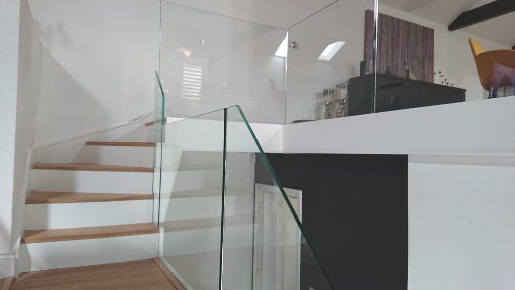 A white frameless glass staircase in a large open plan Lewisham living space.
