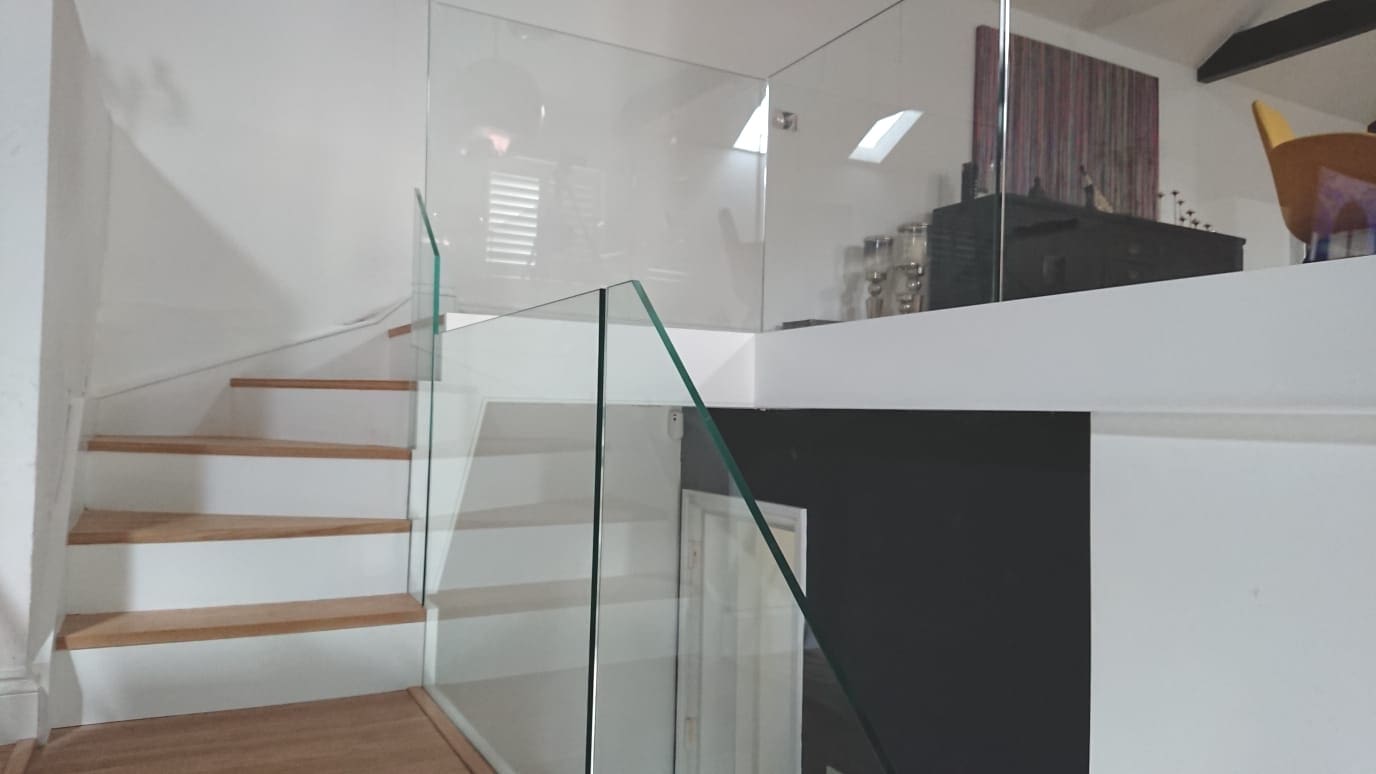 A white frameless glass staircase in a large open plan Lewisham living space.
