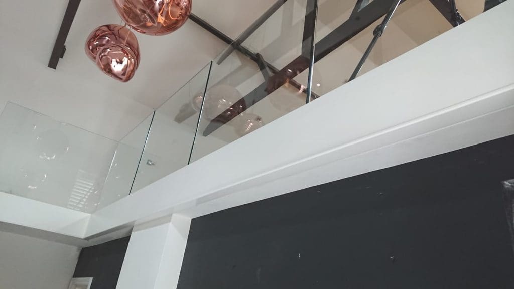 A white frameless glass staircase in a large open plan Lewisham living space.