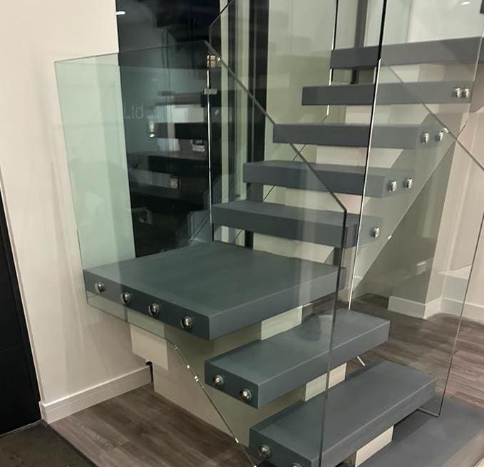 A modern central single spine staircase with a quarter landing in contrasting colours and 15mm Frameless Glass balustrade installed in Towcester.