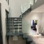 A modern central single spine staircase with a quarter landing in contrasting colours and 15mm Frameless Glass balustrade installed in Towcester.